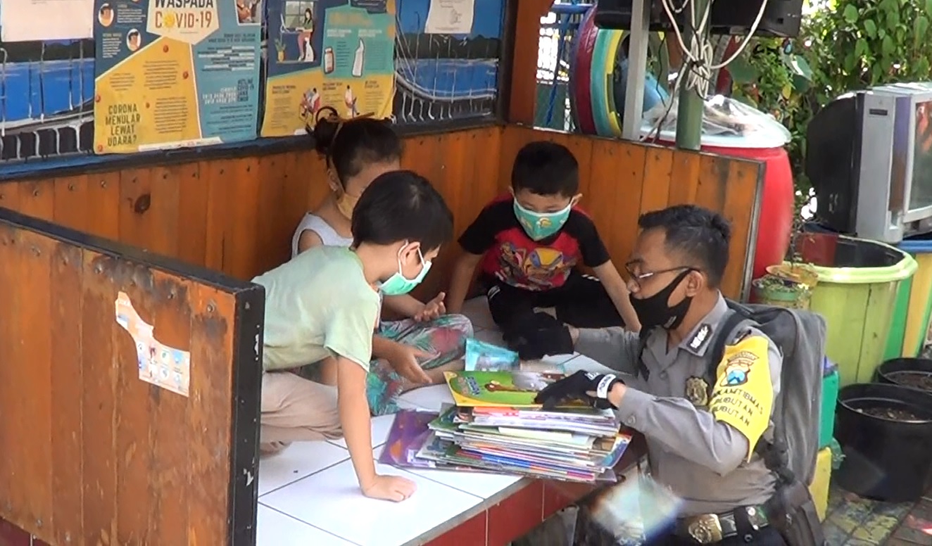 Anggota Babinkamtibmas Polsek Bubutan, Surabaya membagikan ratusan buku untuk mengusir ke junuhan anak selama pandemi (foto/metro)