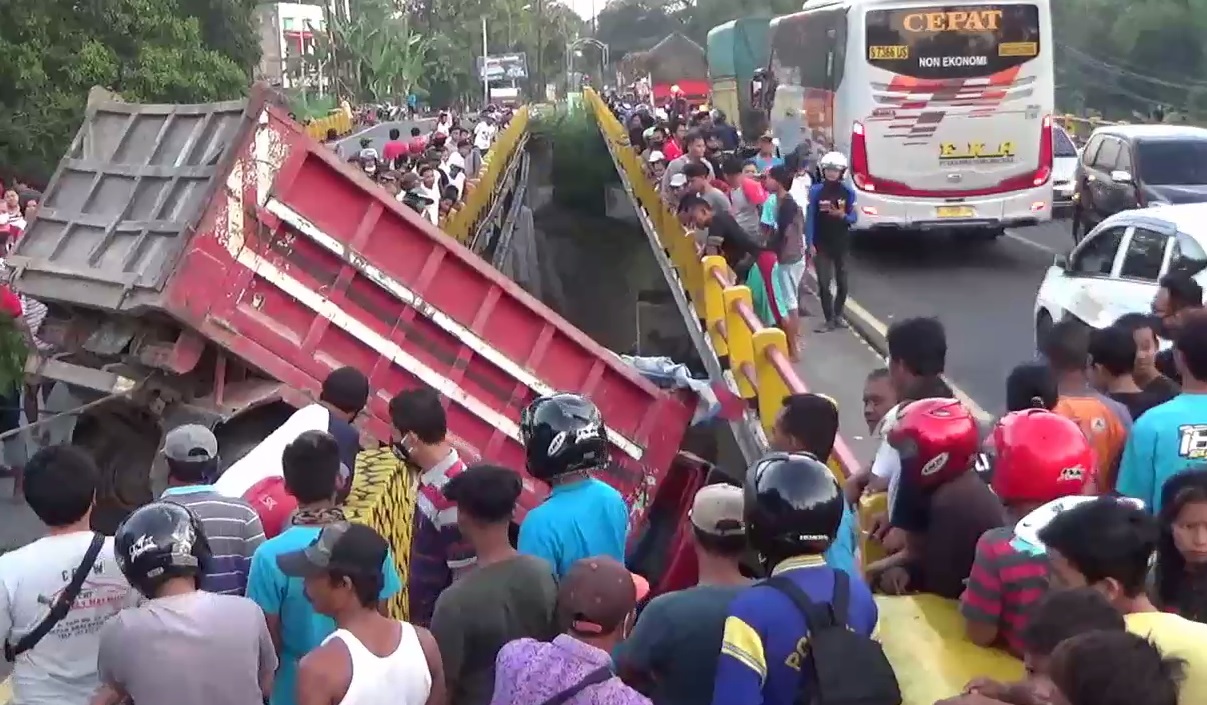 Separuh badan truk yang  sudah masuk ke kolong jembatan menjadi tontotan warga. (foto/metrotv) 