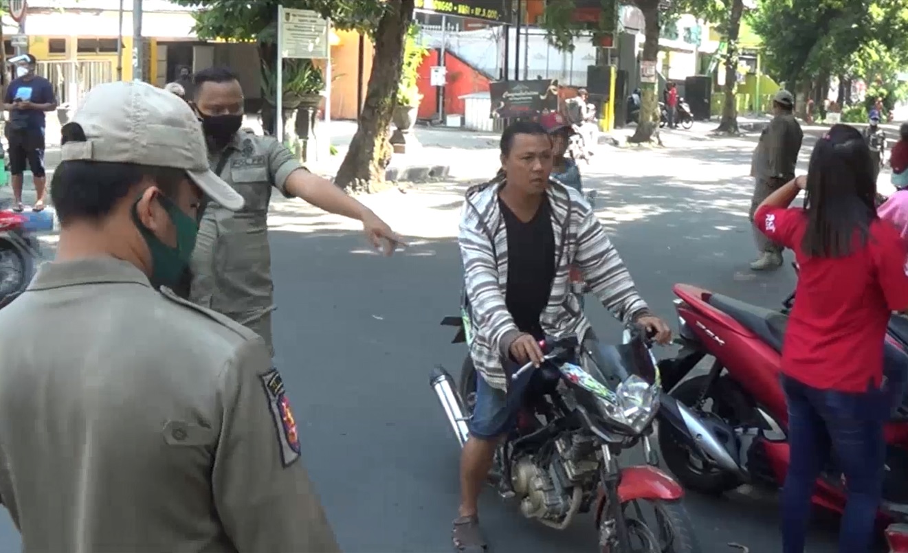 Petugas menghentikan pengendara motor yang tidak memakai masker saat melintas di sekitar Alun-alun Jombang. (foto/metrotv)