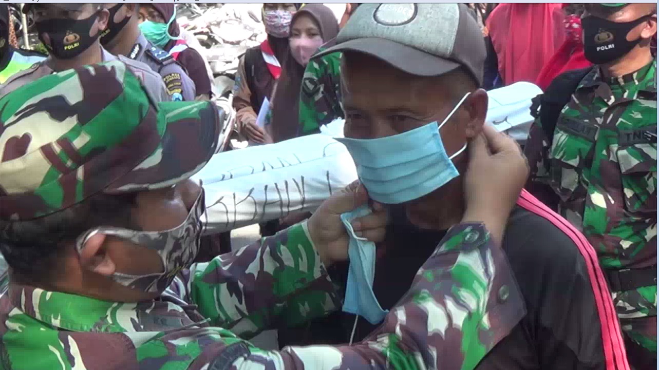 Anggota TNI dan Polri membagikan masker sambil mengotong replika mayat korban covid-19