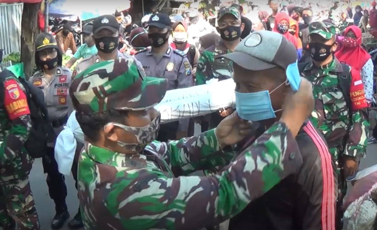 Petugas gabungan terdiri dari TNI dan Polisi di Kabupaten Jombang membagikan masker sambil membawa mayat korban korona (Foto / Metro TV)