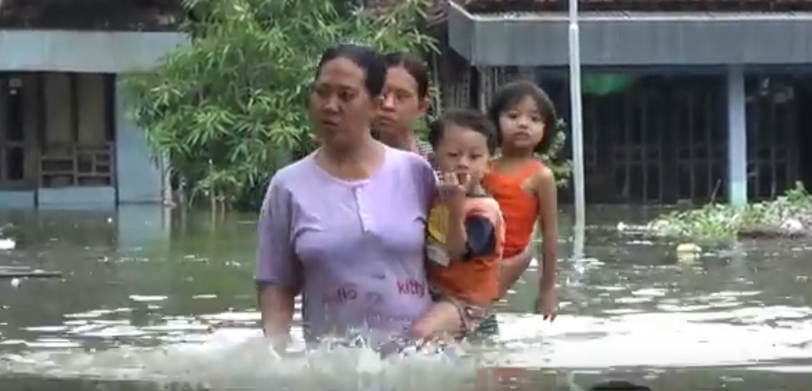 Dua orang ibu sedang menggendong anaknya di tengah terjangan banjir luapan Kali Lamong (Foto / Metro TV)