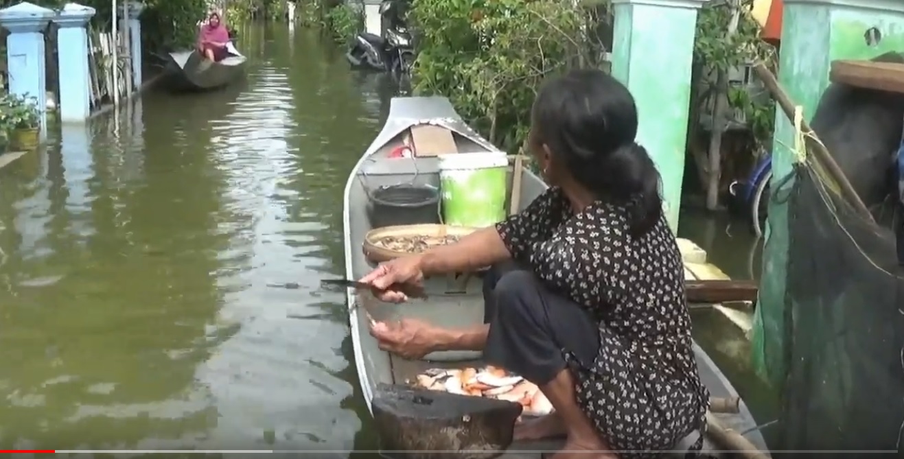 Seorang ibu sedang memberishkan ikan di atas sampan depan rumah akibat banjir yang tak kunjung surut (Foto / Metro TV) 