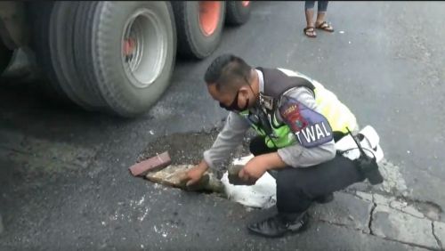 Anggota Polantas Polres Tuban melakukan perbaikan darurat di sambungan Jembatan Merik  yang berlubang. (metrotv)