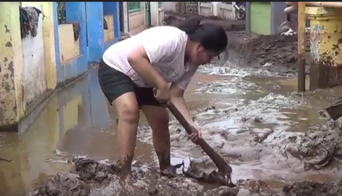 Seorang ibu susah payah membersihkan lumpur akibat banjir di wilayah Probolinggo. (metrotv)