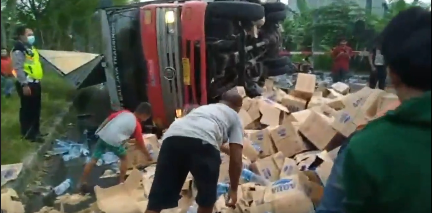 Warga membantu menyingkirkan ratusan kardus air mineral yang berserakan di jalan setelah truk dihantam kereta (Foto / Metro TV)