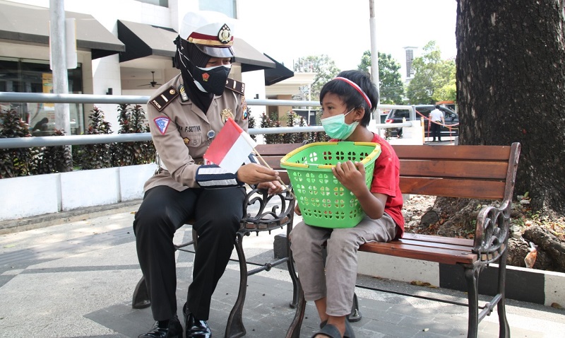 Salah satu polwan anggota Satlantas Polres Malang membagikan bendera merah putih kepada salah satu anak pedagang asongan (Foto / Metro Tv)