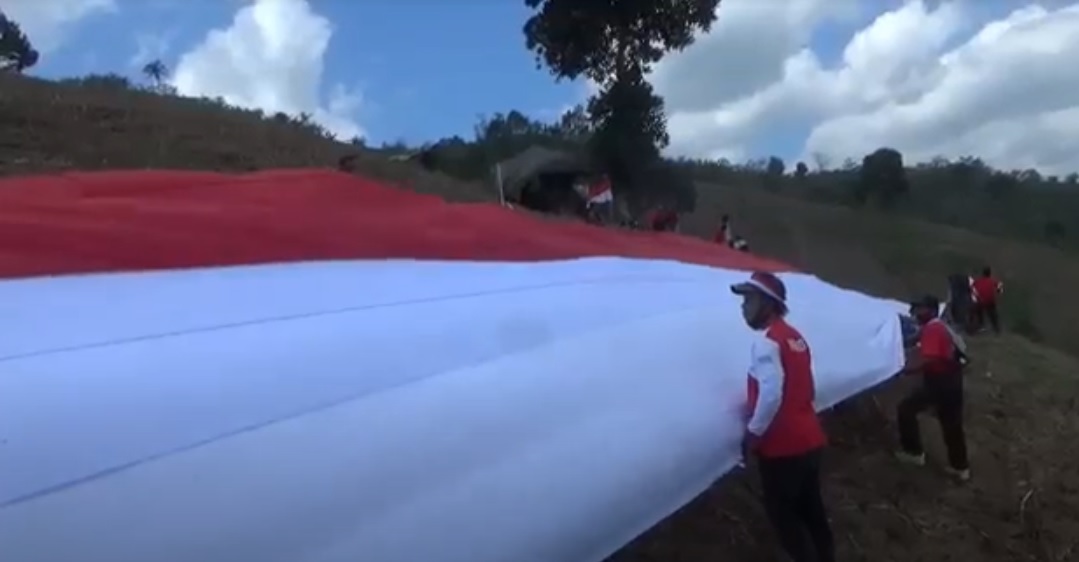 Warga Desa Lampeji, Kecamatan Mumbulsari, Kabupaten Jember, bergotong royong membentangkan bendera raksasa di kawasan perbukitan hutan lindung. (metrotv)