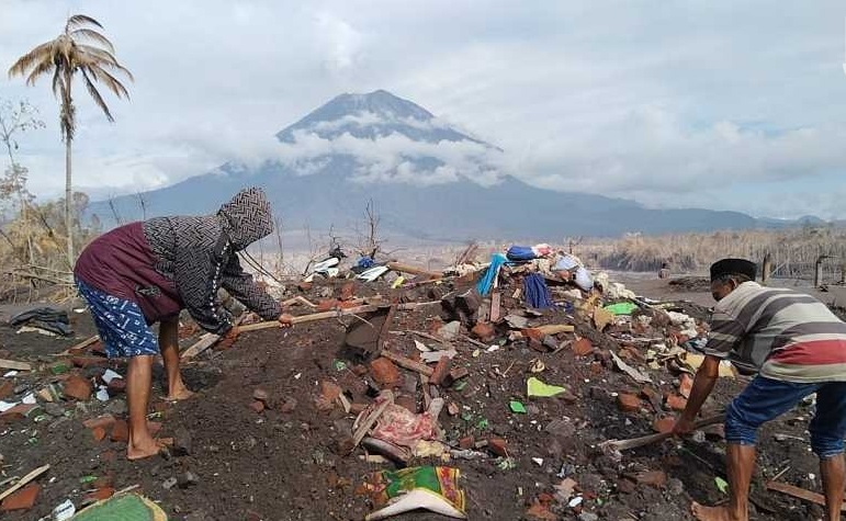 Radi dan anaknya mencari barang-barang berharga yang mungkin tersisa di reruntuhan rumahnya yang hancur disapu erupsi Gunung Semeru (Foto / Istimewa)