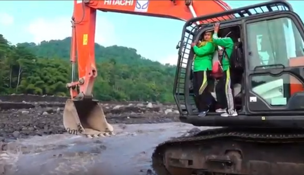 Eriwati dan guru lainnya menyeberangi jalur lahar berarus deras menggunakan ekskavator. (metrotv)