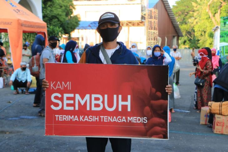 Seorang warga yang dinyatakan sembuh dari covid-19 membawa spanduk bertuliskan ucapan terima kasih kepada tenaga medis saat dipulangkan dari tempat karantina di Asrama Haji Surabaya. Dok. Foto: Antara/HO-Diskominfo Surabaya