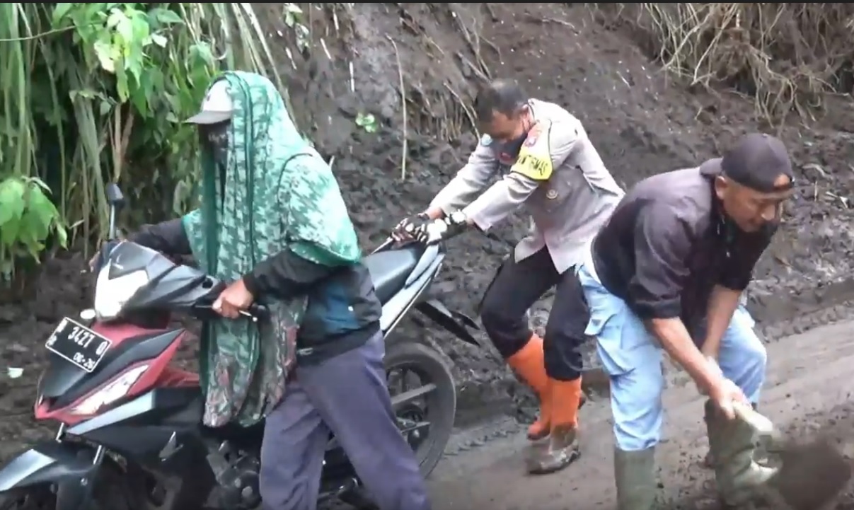 Petugas kepolisian membantu pengendara roda dua melintasi jalur licin setelah terjadi longsor/metrotv