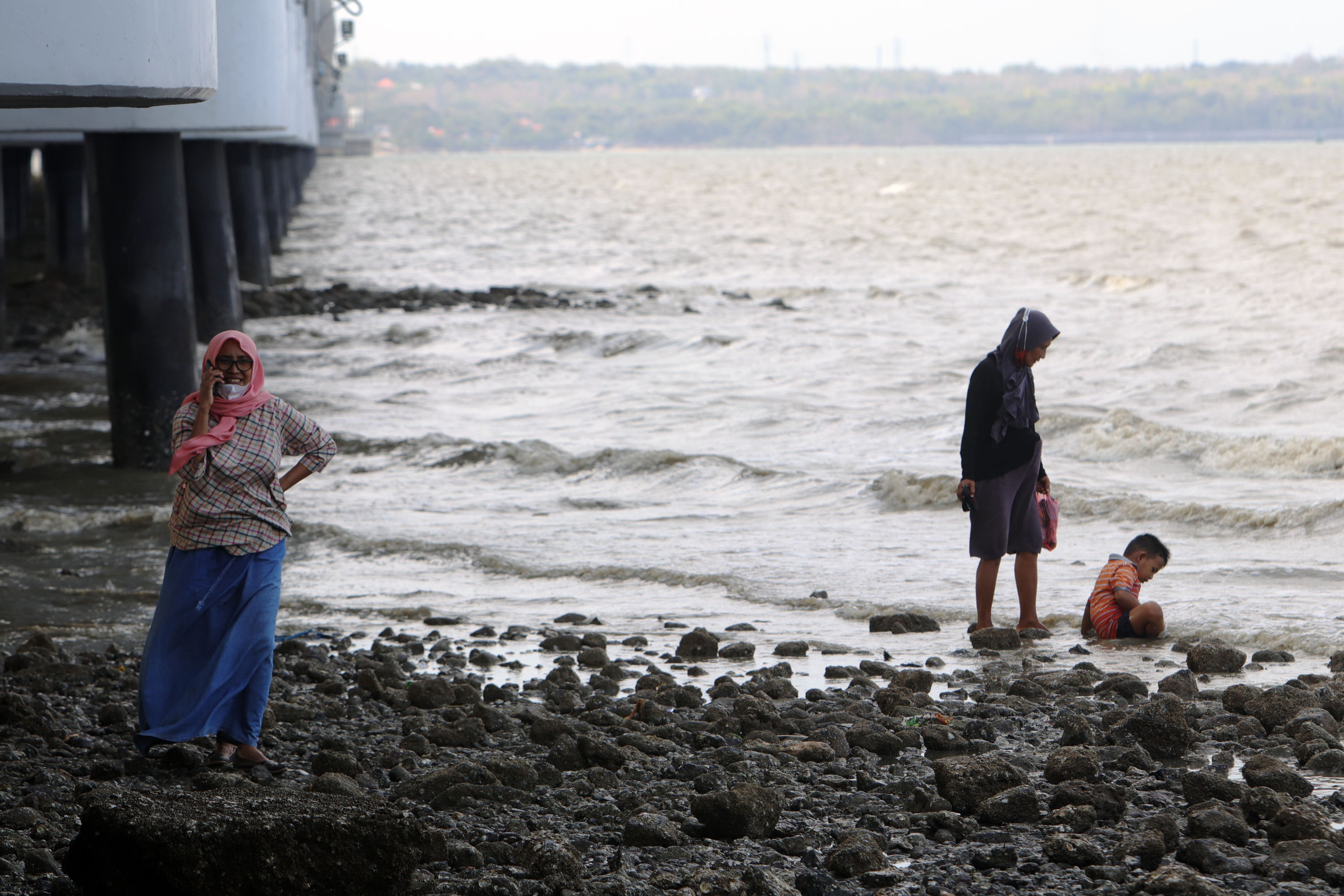 KOMUNIKASI: Warga melakukan panggilan saat menikmati waktu di pantai kaki jembatan Suramadu, Surabaya, Rabu (8/9). Jaringan telkomsel 5G diharapkan bisa menghadirkan akses konektivitas digital terdepan yang akan semakin yang lebih luas, termasuk dalam hal
