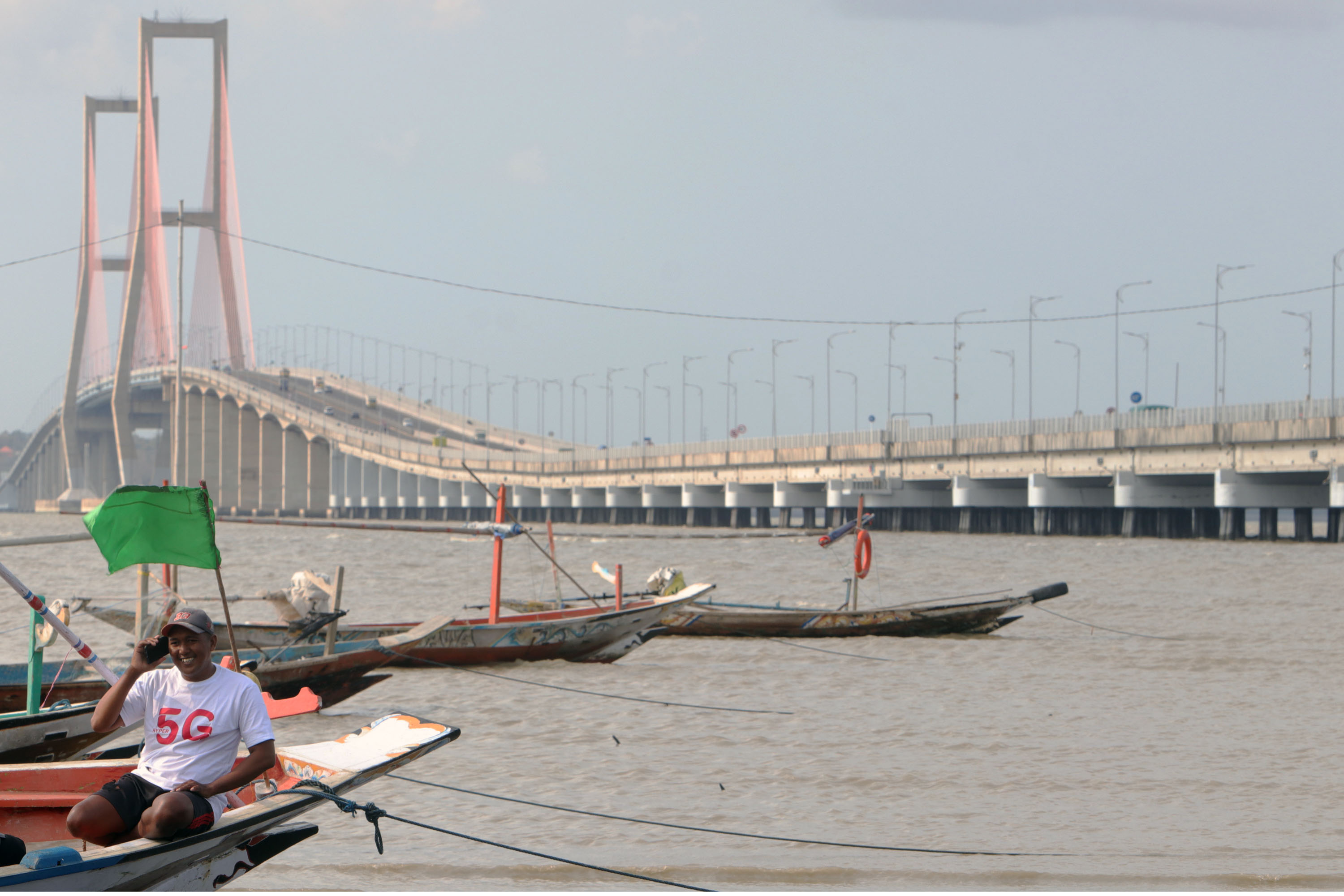 JARINGAN LANCAR: Nelayan di kawasan pesisir pantai Surabaya (kaki jembatan Suramadu), melakukan panggilan kepada kerabatnya, Rabu (8/9). Jaringan telkomsel 5G diharapkan bisa menghadirkan akses konektivitas digital terdepan (Foto / Yuan / Medcom.id)